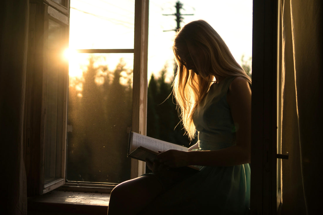 woman reading a book by a window with natural sunset light
