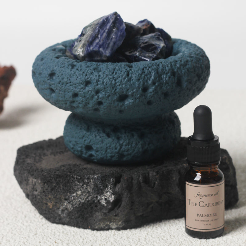 Blue Moon Vessel diffuser with crystals displayed on stone beside Caribbean fragrance oil